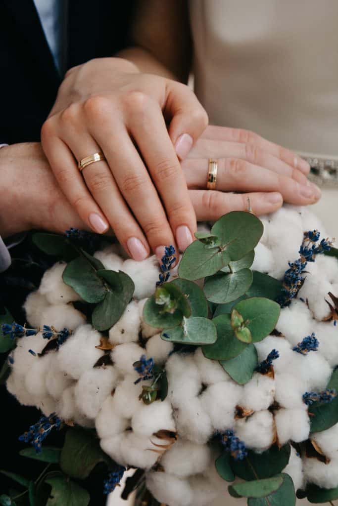 Bride and Grooms hands, wearing wedding rings with bridal bouquet.