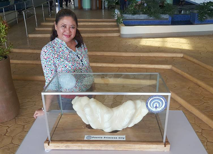 Woman standing next to big pearl in a glass case